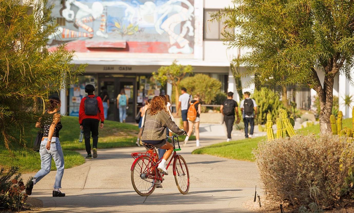 several students walk across the mounds with mead hall entrance in the background